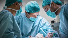   Three healthcare providers in scrubs performing surgery on a patient