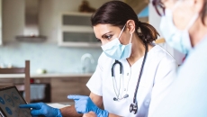   Healthcare providers in lab coats wearing a mask and stethoscope and looking at a screen