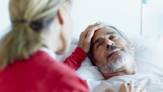 Person in a red shirt sitting next to someone in a hospital gown lying in a bed