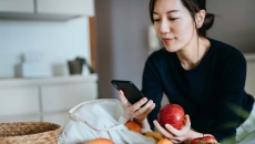 Person leaning against a counter holding an apple while looking at their phone
