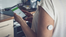 A person wearing a CGM patch checking their blood glucose level on a mobile app