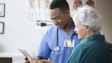 Healthcare professional standing next to a patient while holding a tablet Healthcare professional standing next to a patient while holding a tablet