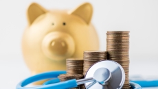 A piggy bank next to coins and a stethoscope A piggy bank next to coins and a stethoscope