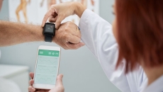 A doctor helping a patient sync heart rate data from a wearable to a smartphone.