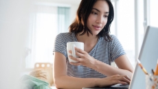 Person sitting at their computer while holding a cup of coffee