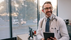Doctor leaning against a desk while holding a tablet