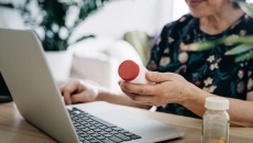 A woman holding a pill bottle using a laptop A woman holding a pill bottle using a laptop