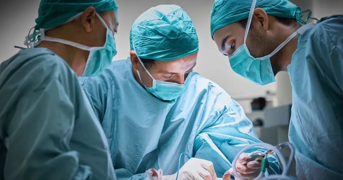   Three healthcare providers in scrubs performing surgery on a patient